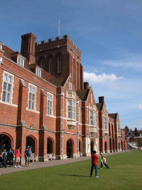 Estudantes à frente de um edifício histórico de tijolos vermelhos com uma torre, num ambiente inspirador para um curso de língua inglesa.