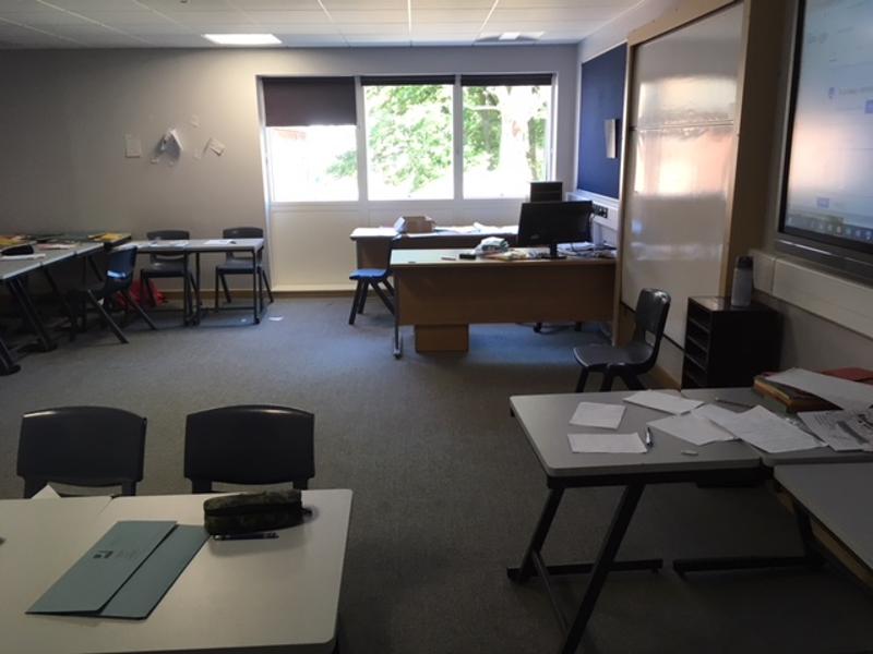 Sala de aula com mesas, cadeiras e quadro interativo, preparada para receber alunos de um curso de língua inglesa.