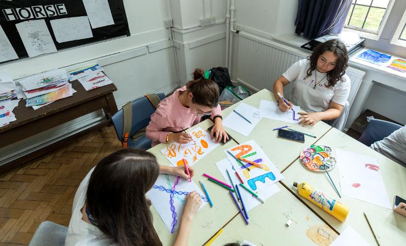 Estudantes a criar trabalhos artísticos com lápis e tintas durante uma atividade criativa no curso de língua inglesa.