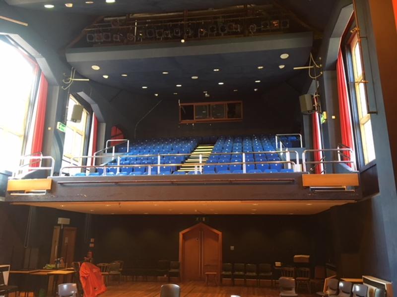 Teatro vazio com assentos azuis e palco de madeira, utilizado durante o curso de inglês no Reino Unido.