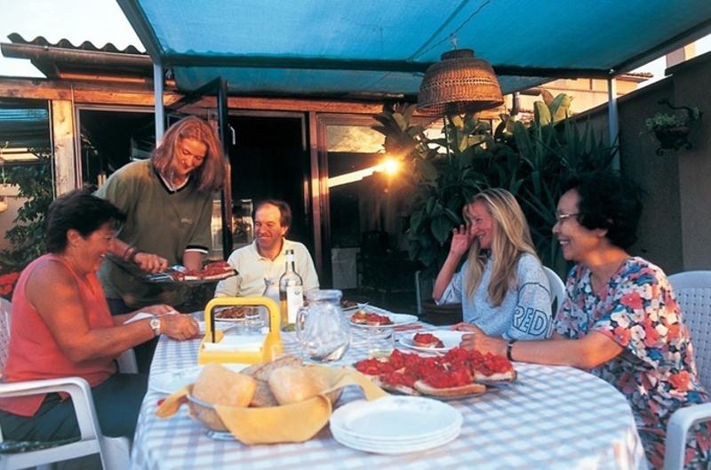 Grupo de pessoas a desfrutar de uma refeição ao ar livre, partilhando pratos tradicionais, durante um curso italiano.