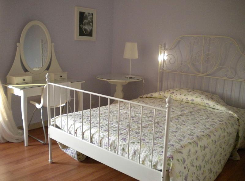 Quarto decorado em tons suaves com cama de ferro forjado e toucador, ideal para relaxar durante o curso italiano.