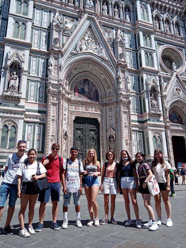 Grupo de estudantes em frente a uma catedral histórica durante um curso italiano, explorando a cultura e história local.