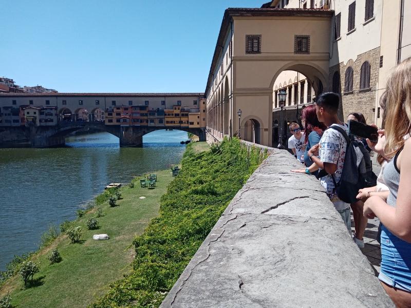 Grupo de estudantes a admirar a Ponte Vecchio durante um curso italiano, explorando a rica história local.