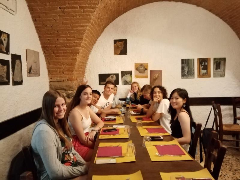 Grupo de estudantes sentados num restaurante tradicional, a desfrutar de uma experiência gastronómica durante um curso italiano.
