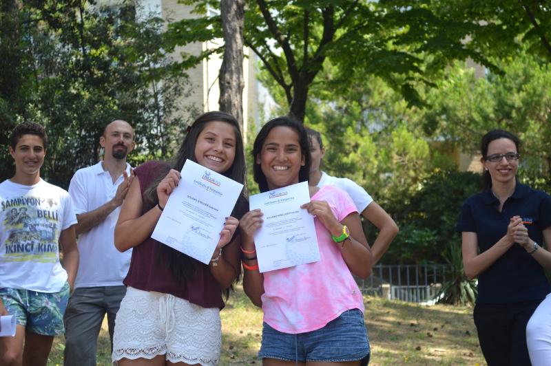 Duas jovens a exibir certificados de conclusão após participarem num curso italiano.