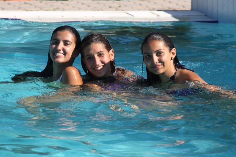 Três jovens a divertir-se numa piscina durante um curso italiano, aproveitando momentos de lazer.