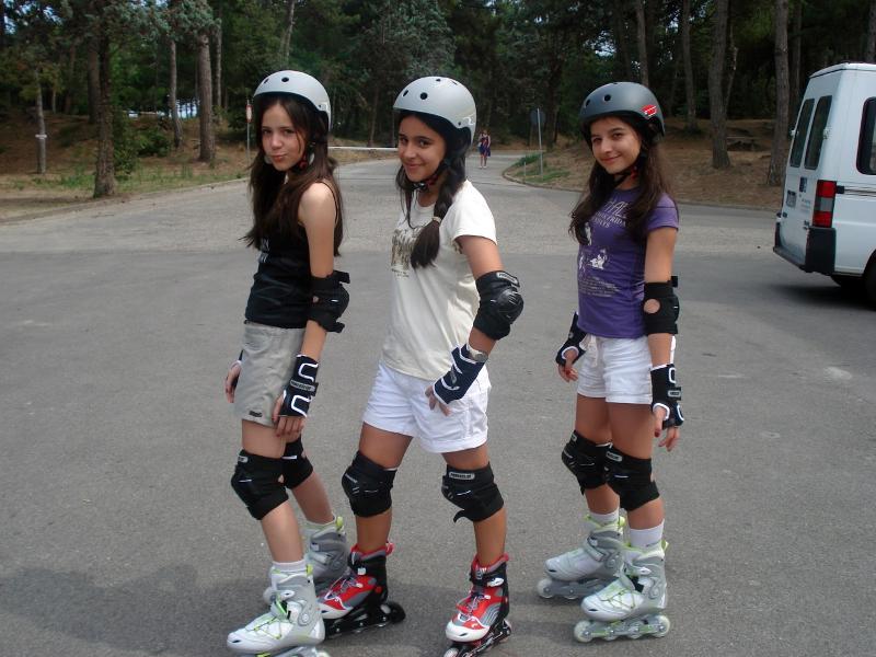 Três jovens com capacetes e proteções, a andar de patins enquanto praticam um curso italiano.