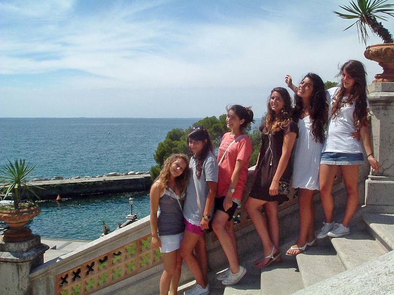 Grupo de jovens sorridentes a tirar uma foto em frente ao mar, durante um evento relacionado com o curso italiano.