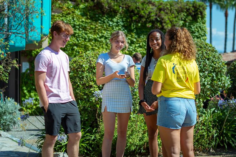 Grupo de jovens a conversar ao ar livre durante um curso de língua francesa, com plantas ao fundo