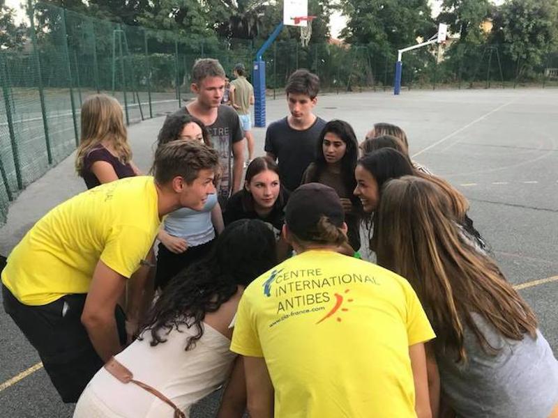 rupo de jovens a participar em uma atividade interativa, reunindo-se em círculo sob a orientação de um monitor do Centre International d'Antibes durante o curso de lingua francesa