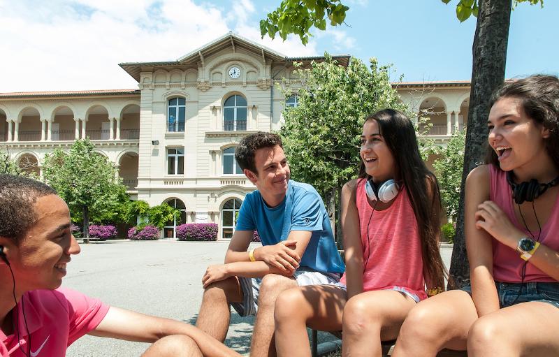 Grupo de jovens sentados ao ar livre a sorrir e a conversar num ambiente descontraído durante um curso de língua francesa