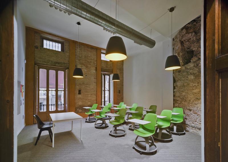 Sala de aula moderna com cadeiras verdes e janelas grandes, preparada para receber alunos de um curso de espanhol.
