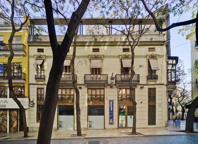 Fachada de um edifício histórico com amplas janelas e detalhes arquitetónicos clássicos, onde é realizado um curso de espanhol.