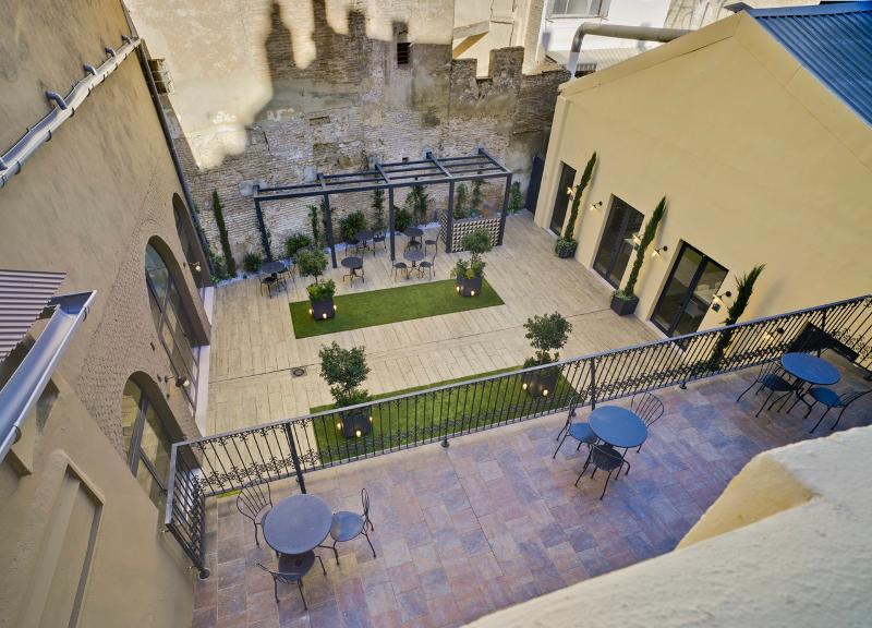 Vista aérea de um pátio espaçoso com mesas, cadeiras e áreas verdes, proporcionando um ambiente relaxante para estudantes de um curso de espanhol.