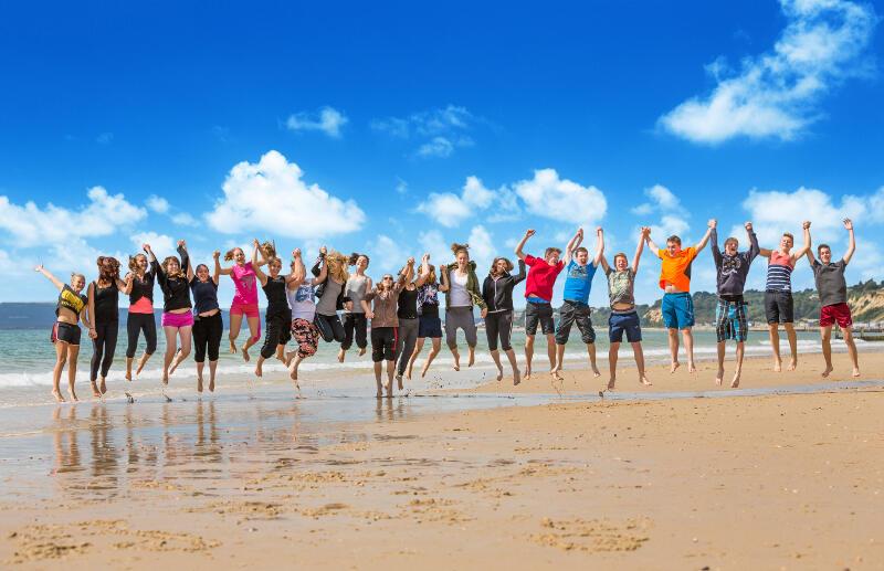 Participantes de mão dada a darem um salto na praia no curso de línguas malta