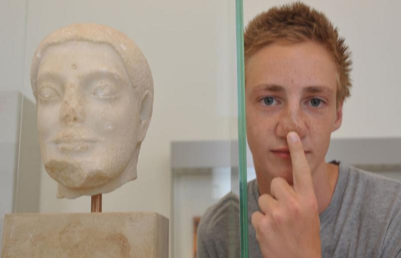 Rapaz ao lado de uma estátua de uma cabeça, capturando a arte e cultura enquanto faz o seu curso de inglês na alemanha.