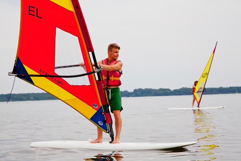 Rapaz a praticar windsurf em águas agitadas, com céu nublado, enquanto aproveita a aventura durante o seu curso de inglês na alemanha.