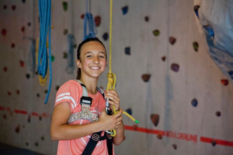 Rapariga sorridente com uma blusa rosa, a praticar climbing indoor, desfrutando de uma atividade física enquanto faz o seu curso de inglês na alemanha.