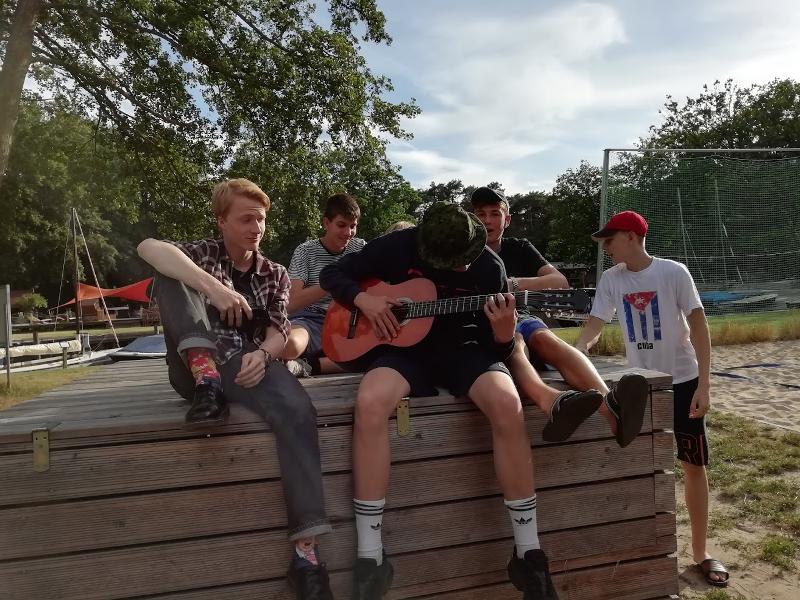 Cinco jovens sentados num jardim, com um deles a tocar guitarra, aproveitando o tempo livre durante o seu curso de inglês na alemanha.