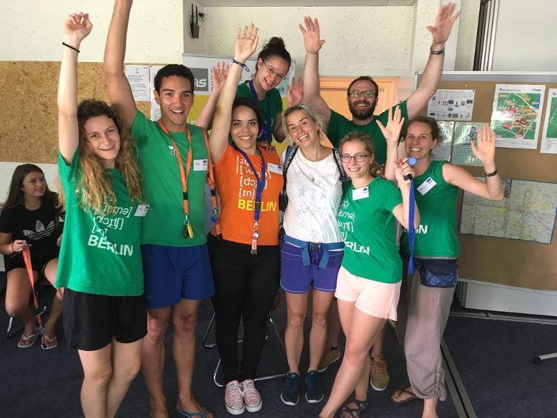 Grupo de participantes a sorrir e com as mãos no ar, celebrando a diversão e a aprendizagem no seu curso de inglês na alemanha.