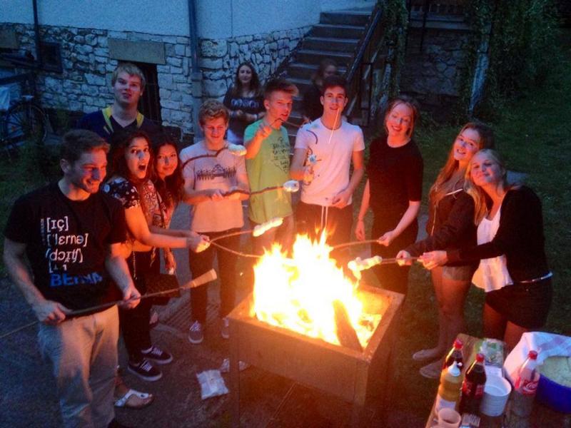 Grupo de estudantes a fazer um barbecue numa fogueira, aproveitando a noite ao ar livre durante o seu curso de inglês na alemanha.