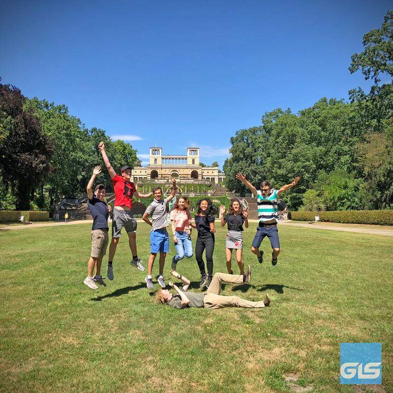 Grupo de estudantes a saltar para a foto na relva, a aproveitar o dia de sol durante o seu curso de inglês na alemanha.