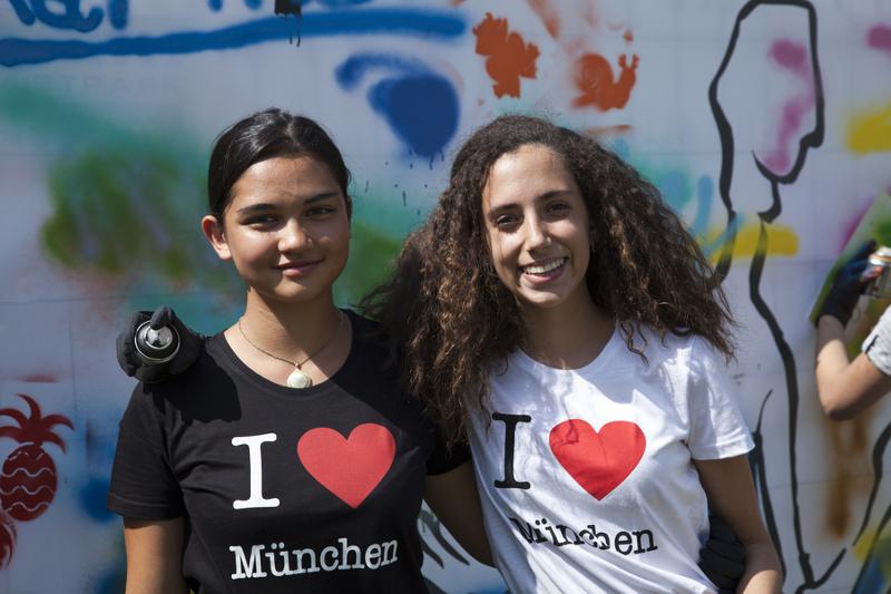 Duas participantes com blusa "I love Munich" a sorrir, a desfrutar da experiência no seu curso de inglês na alemanha.