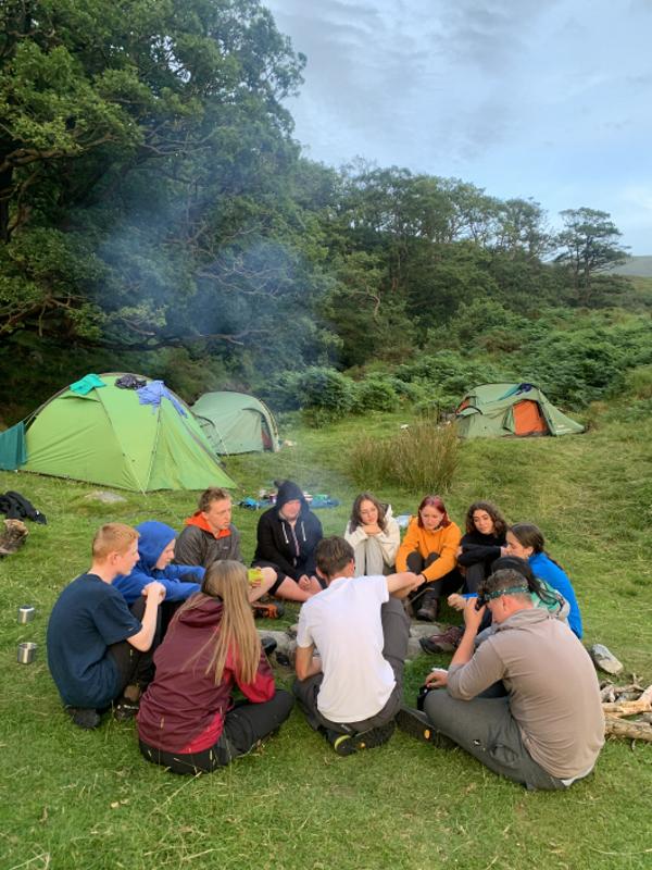 Grupo de jovens a comer juntos no chão, acampando e desfrutando da experiência enquanto fazem o seu curso de ingles na irlanda.