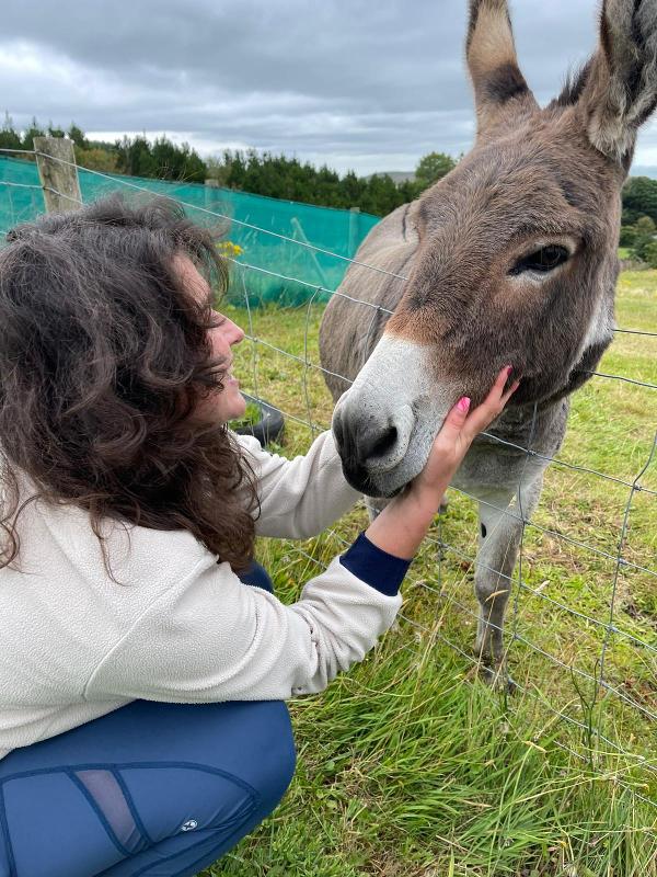 Jovem ao lado de um burro, desfrutando da companhia do animal enquanto faz o seu curso de ingles na irlanda.