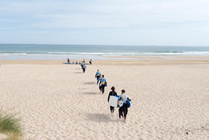 Jovens a caminhar em direção à praia com as pranchas de surf, prontos para surfar enquanto fazem o seu curso de ingles na irlanda.