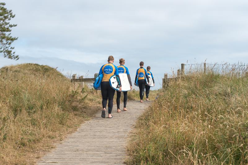 Jovens a caminhar em direção à praia com as pranchas de surf, prontos para aproveitar as ondas enquanto fazem o seu curso de ingles na irlanda.