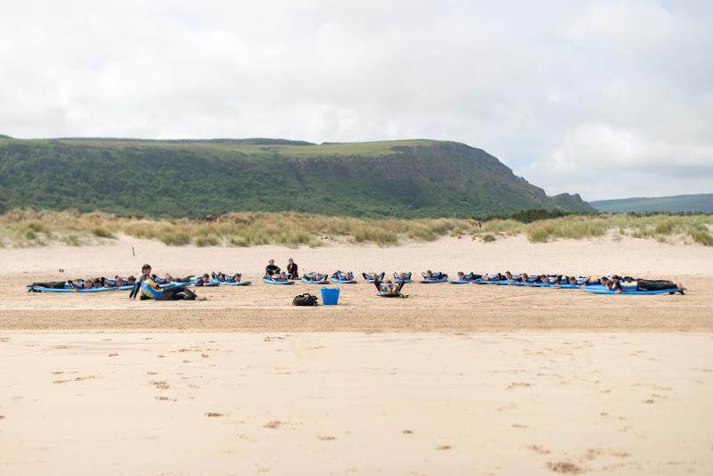 Jovens deitados na areia com pranchas de surf à sua volta, a relaxar na praia enquanto fazem o seu curso de ingles na irlanda.