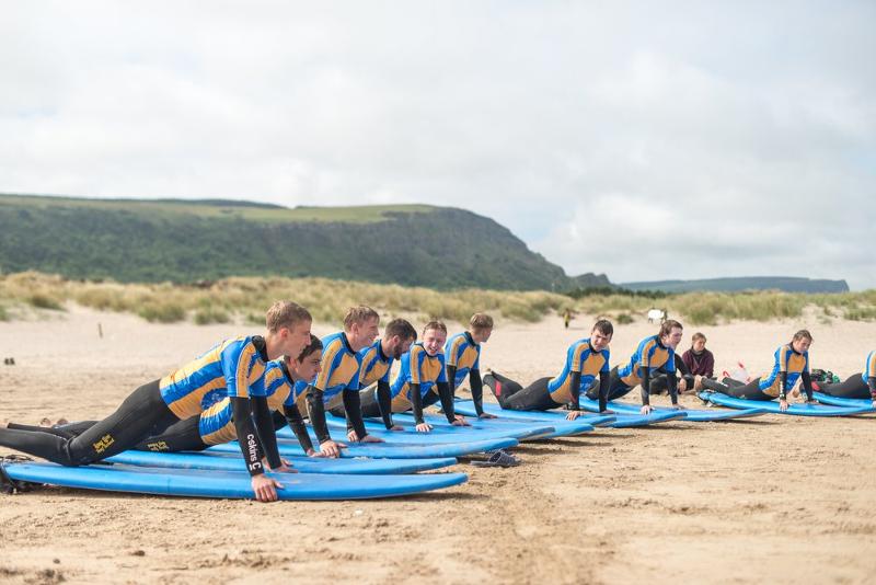 Jovens na praia com pranchas de surf na areia, prontos para apanhar as ondas enquanto fazem o seu curso de ingles na irlanda.