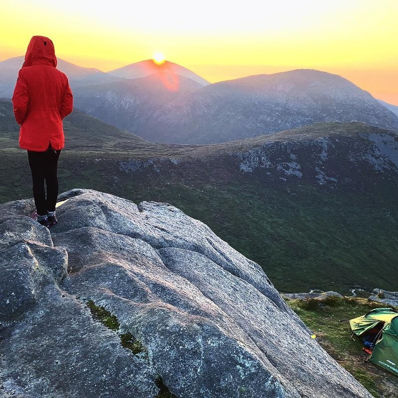 Jovem a contemplar o pôr do sol na montanha, a aproveitar o momento de paz enquanto faz o seu curso de ingles na irlanda.