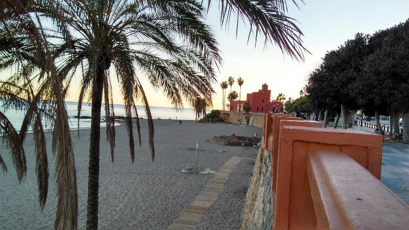 Praia serena ao pôr do sol com palmeiras e edifício histórico, ideal para um curso de lingua espanhola junto ao mar.