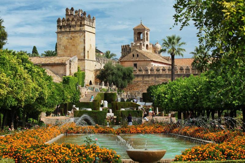 Jardins exuberantes com fontes e flores vibrantes ao lado de uma antiga fortaleza, um cenário inspirador para um curso de lingua espanhola.