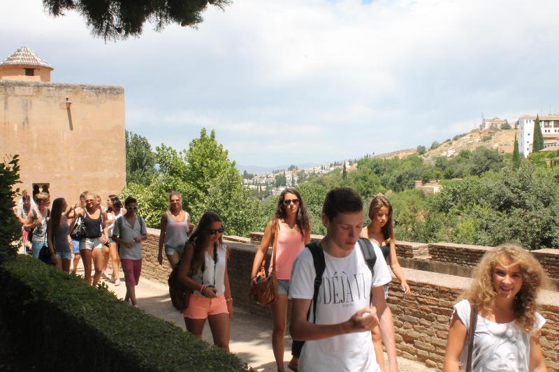 Grupo de jovens a caminhar por um cenário histórico com vista para colinas, explorando a cultura durante um curso de lingua espanhola.