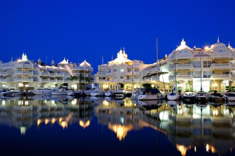 Marina iluminada à noite com edifícios refletidos na água, criando um ambiente mágico para um curso de lingua espanhola.