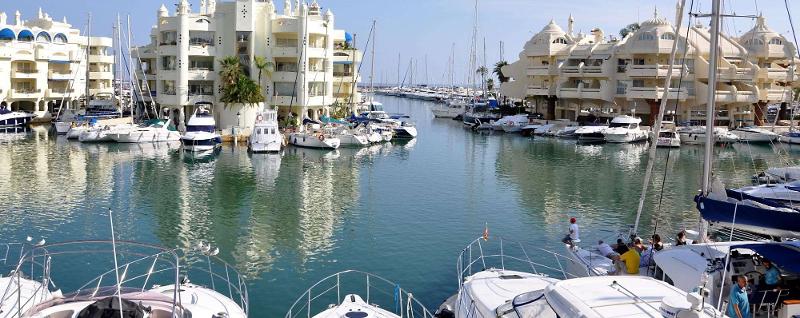 Marina com barcos ancorados cercada por edifícios elegantes e céu azul, um cenário relaxante para um curso de lingua espanhola.