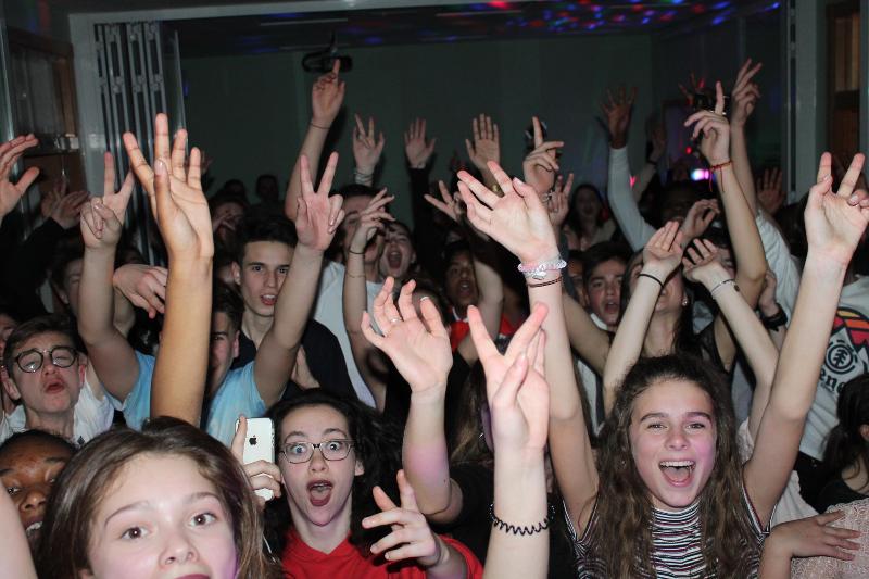 Grupo de jovens a celebrar com entusiasmo numa festa, desfrutando da interação social proporcionada por um curso de lingua espanhola.