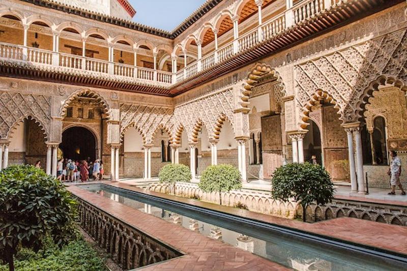 Pátio interno de um palácio com arcos decorados e um canal de água central, oferecendo um ambiente histórico para um curso de lingua espanhola.