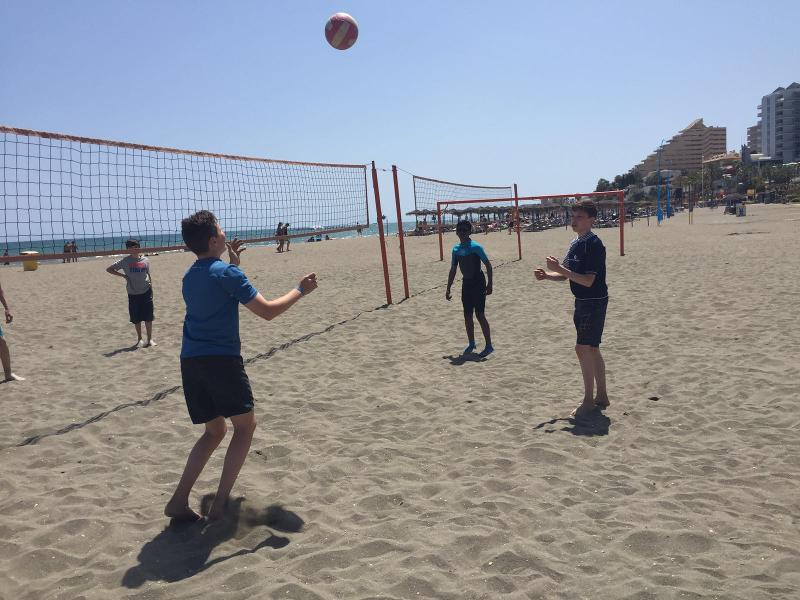 Jovens a jogar voleibol na praia, aproveitando o sol e atividades desportivas durante um curso de lingua espanhola.