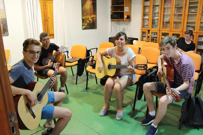 Estudantes a tocar guitarra e ukulele em grupo durante uma atividade cultural num curso de espanhol.
