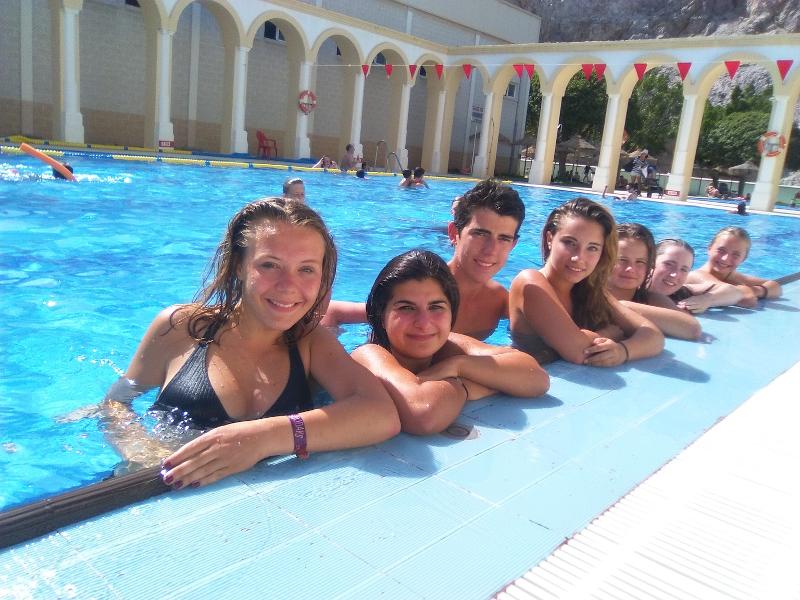 Grupo de estudantes sorridentes na borda de uma piscina, aproveitando o tempo livre durante um curso de espanhol.