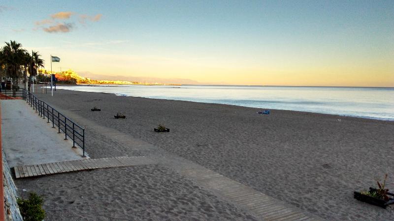 Praia tranquila ao amanhecer, com um caminho de madeira e palmeiras, ideal para relaxar depois dos cursos de linguas em espanha.