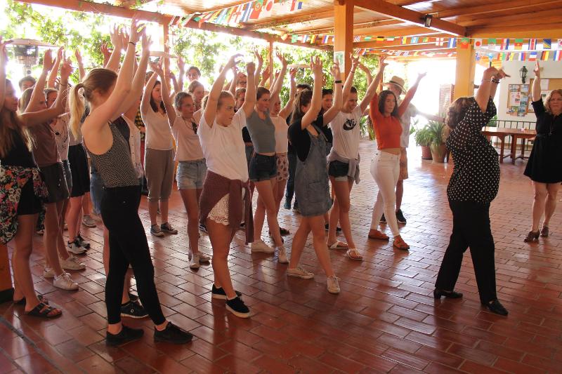Grupo de estudantes participando numa aula de dança, com os braços levantados, enquanto aprendem e se divertem nos cursos de linguas em espanha.