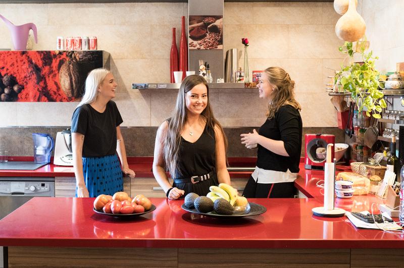 Três raparigas numa cozinha moderna a rir e felizes durante o curso de língua espanhola